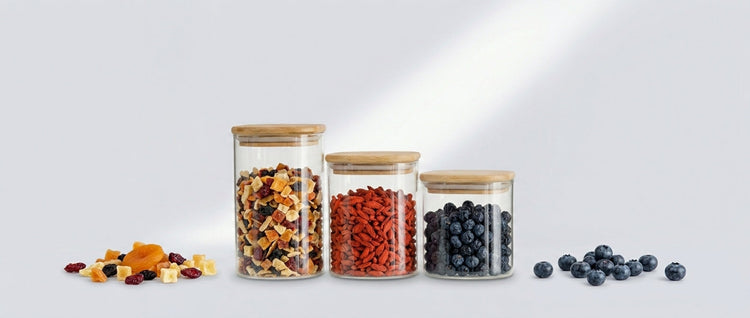 Three square glass jars with bamboo lids holding dried fruit, goji berries and blueberries